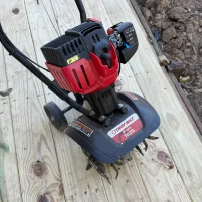 Sale Photo Thumbnail #200: Troy-Bilt TB225 2-cycle garden cultivator tiller resting on a wooden deck, showing light wear.