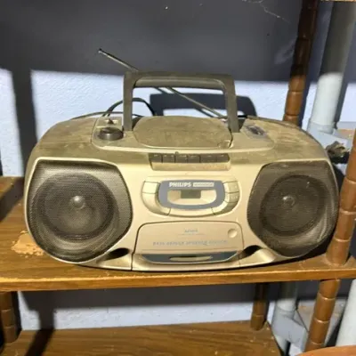 Sale Photo Thumbnail #401: Vintage dusty silver Philips Magnavox portable boombox with CD player, cassette deck, and AM/FM radio, sitting on a wooden shelf.