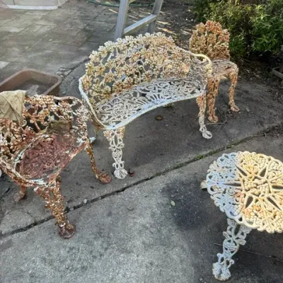 Sale Photo Thumbnail #494: Vintage ornate cast aluminum four-piece patio set featuring a bench, two side chairs, and a round accent table, all displaying heavy rust and weathered white paint.