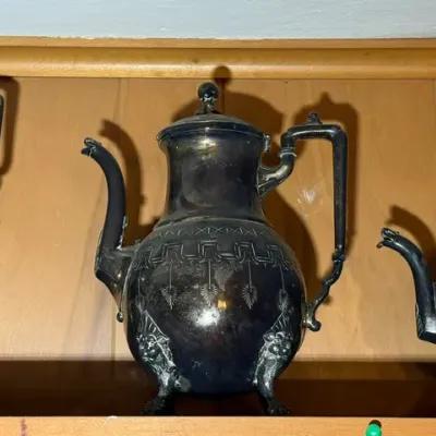 Sale Photo Thumbnail #270: Vintage silver-plated teapot featuring intricate engraved geometric band detailing and ornate lion paw feet, displaying significant surface tarnish.