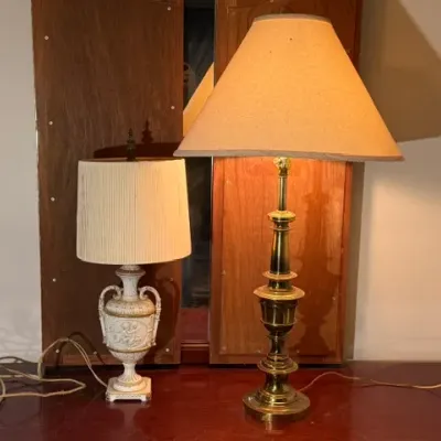 Sale Photo Thumbnail #165: Two vintage table lamps, including a smaller classical urn-style porcelain lamp with relief detail and a taller brass candlestick-style lamp, both featuring fabric shades.