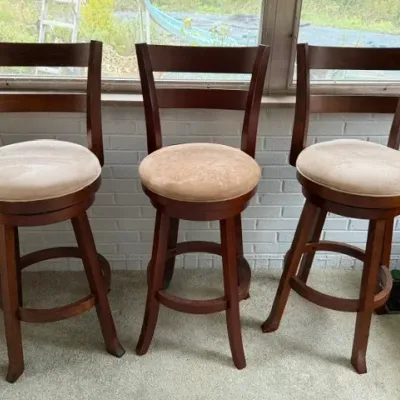 Sale Photo Thumbnail #172: Set of three contemporary wooden swivel bar stools featuring ladder-back designs, round cushioned seats in light beige suede, and circular footrests.
