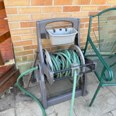 Sale Photo Thumbnail #498: Gray plastic mobile hose reel cart with a green garden hose attached, paired with a small storage basket.