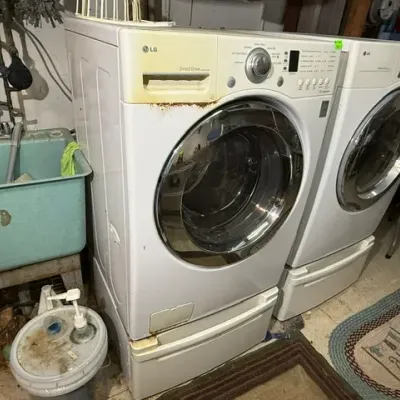 Sale Photo Thumbnail #386: LG Direct Drive front-load washing machine and matching dryer set on pedestal drawers, showing heavy rust and yellowing on the washer housing.