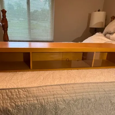 Sale Photo Thumbnail #150: Long, low light oak shelf unit with glass sliding doors and open side compartments resting on a bed.