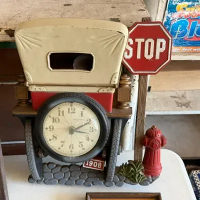 Sale Photo Thumbnail #466: Vintage novelty desk clock designed as a 1908 antique automobile, featuring a tire-framed clock face alongside a stop sign and fire hydrant detail.