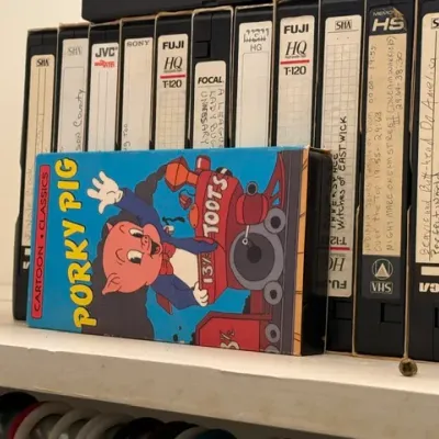 Sale Photo Thumbnail #356: Vintage Porky Pig VHS tape in its original slipcase, displayed in front of a row of home-recorded VHS tapes on a shelf.