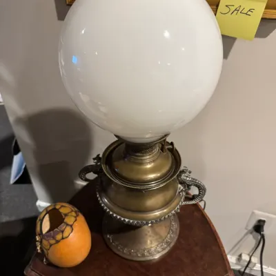 Sale Photo Thumbnail #35: Vintage brass oil-style table lamp with a white globe shade, ornate dragon-shaped side handles, and a glass chimney.
