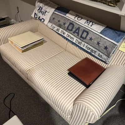 Sale Photo Thumbnail #38: Striped beige and white upholstered sofa featuring rolled arms, draped with a "To My Dad" fleece blanket, photo albums, and leather binders.