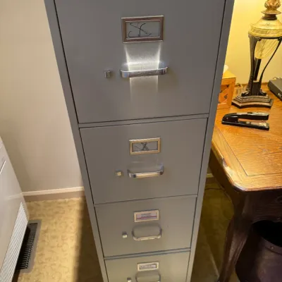 Sale Photo Thumbnail #76: HON grey four-drawer steel vertical filing cabinet with silver handles and label holders.