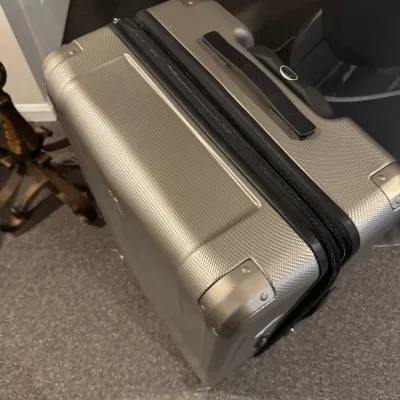 Sale Photo Thumbnail #52: Modern silver hardshell rolling suitcase featuring reinforced corner guards and a black top carrying handle.