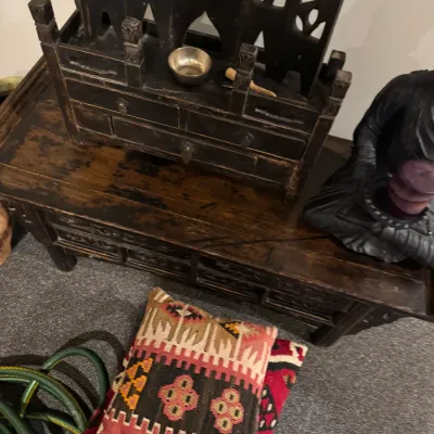 Sale Photo Thumbnail #30: Rustic dark wood Asian-style low table displayed alongside a decorative tabletop shrine, a Buddha statue, and kilim floor cushions.