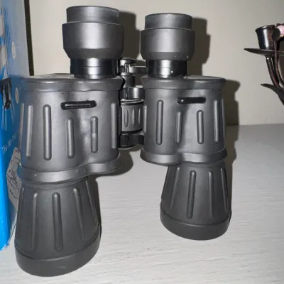 Sale Photo Thumbnail #45: Black rubber-armored binoculars standing upright on a shelf.