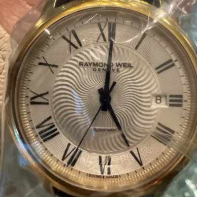 Sale Photo Thumbnail #18: Raymond Weil Geneve automatic wristwatch with a gold-tone case, guilloché pattern dial, black Roman numerals, and date window.