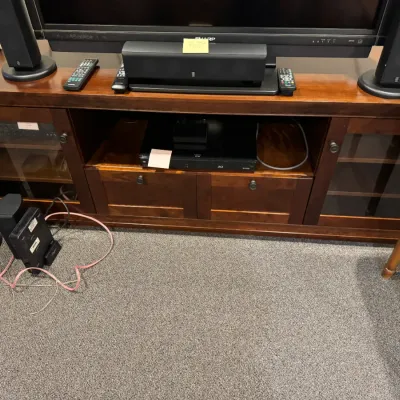 Sale Photo Thumbnail #33: Dark cherry wood media console featuring glass-front cabinets, lower drawers, and open shelving housing electronics and speakers.