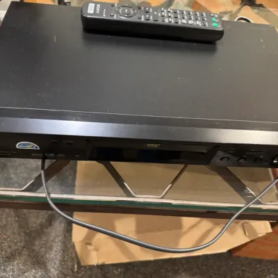 Sale Photo Thumbnail #57: Black Sony DVD player with matching remote control resting on a glass-top table, showing light wear.