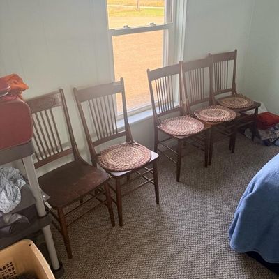 Set of five vintage dark wood spindle-back dining chairs, four featuring woven round seat cushions.