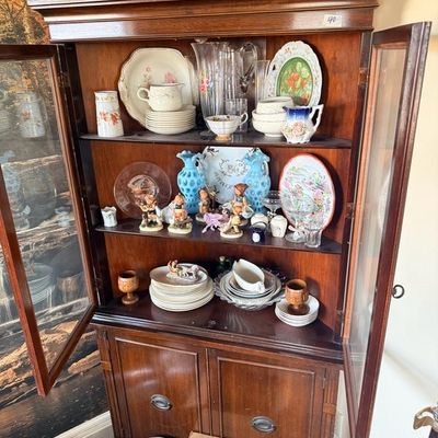 Vintage dark wood china cabinet filled with assorted glassware, Hummel figurines, porcelain dishware, and decorative collectibles.