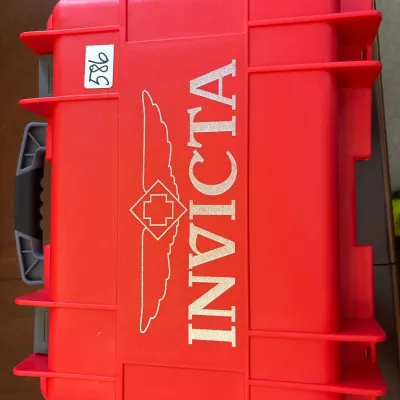 Bright red Invicta hard-shell impact case featuring the brand's logo and winged insignia with a grey carrying handle.