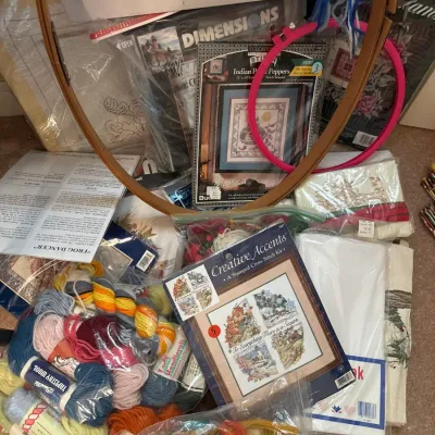 Large assortment of vintage needlepoint and cross-stitch craft supplies, including embroidery hoops, Bucilla tapestry wool yarn, and...