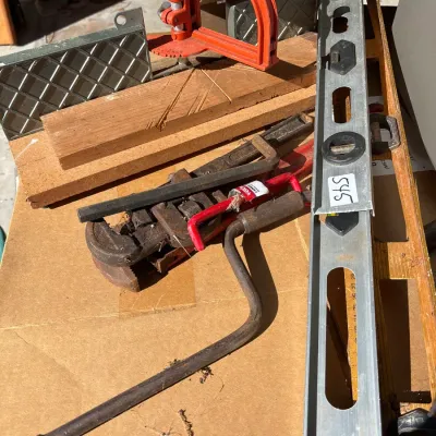 Assortment of vintage hand tools including pipe wrenches, levels, a hand crank, and a miter saw guide set.