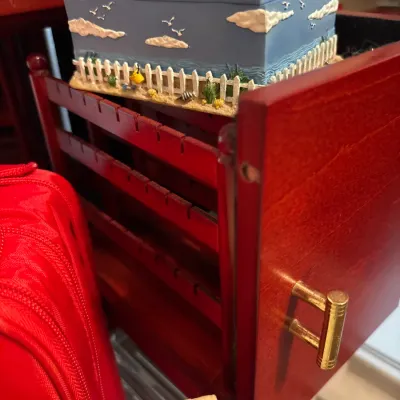 Red wooden jewelry box drawer featuring slotted necklace racks, topped with a beach-themed trinket box.