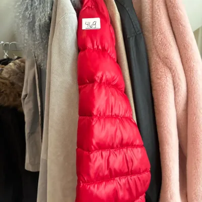 Clothing rack featuring a bright red quilted puffer jacket, a light pink faux fur coat, a light blue curly fur trim coat, and other...