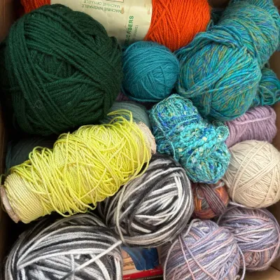 Cardboard box filled with an assortment of yarn skeins and wound balls in various colors and textures.