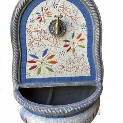 Wall-mounted garden water fountain featuring a colorful floral mosaic design, blue tiled border, and brass spigot.