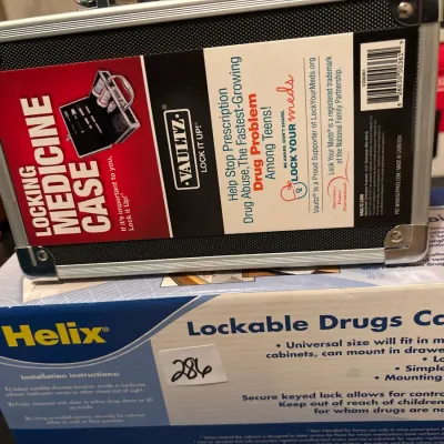 Vaultz locking medicine case with metal trim sitting on top of a Helix lockable drugs cabinet box.