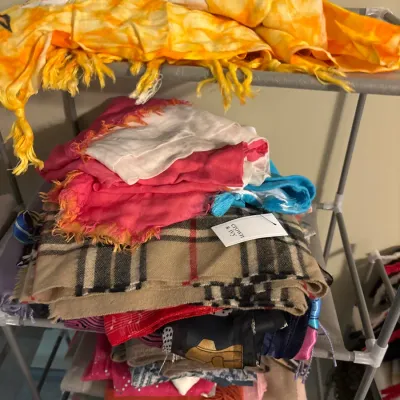 A stack of colorful fabric scarves and wraps on a metal shelving rack, including a Crown & Ivy plaid scarf with tag attached.