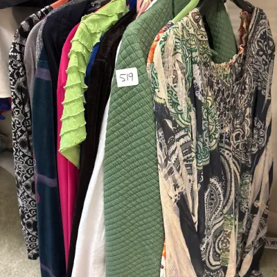 Selection of women's clothing hanging in a closet, featuring a patterned paisley blouse and a quilted green jacket labeled 519.