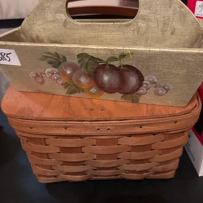 Hand-painted wooden caddy with a crackle finish fruit motif, resting on top of a woven wooden basket with a solid lid.