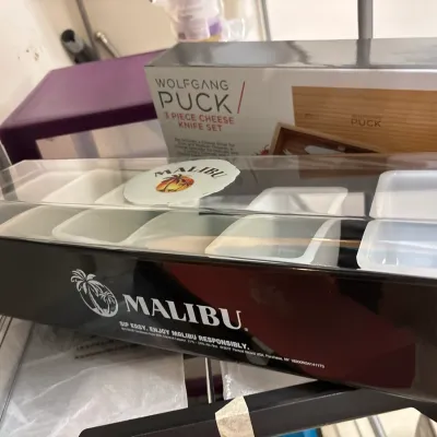 Malibu Rum branded condiment caddy bar organizer alongside a boxed Wolfgang Puck 3-piece cheese knife set.