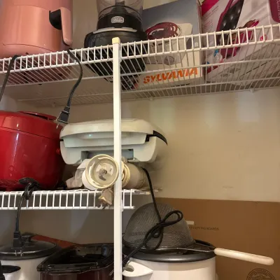 Collection of small kitchen appliances on wire shelving, including a pink air fryer, food processor, rice cookers, slow cooker, and boxed...
