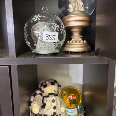 Collection of holiday decorations including an angel snow globe, a glass snowflake orb, a fabric snowman plush, and a Santa snow globe...