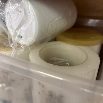 Clear plastic storage tote filled with various white pillar candles and candle-making supplies.