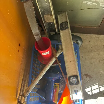 Blue plastic basket containing various hand tools and garage items, including spirit levels, a Proto wrench, a hand saw, and a dumbbell.