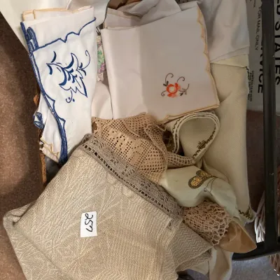 Box lot of vintage household linens featuring embroidered napkins, crocheted trims, and woven table linens.