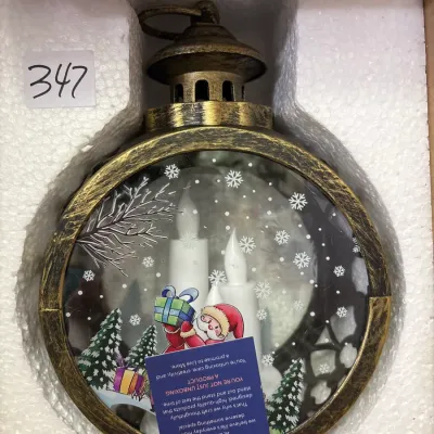 Festive Christmas lantern snow globe with LED flame-shaped candles and a Santa Claus illustration, packaged in its original styrofoam...