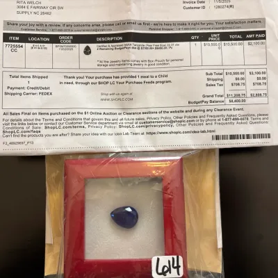 A 22.37-carat pear-cut AAAA tanzanite gemstone displayed in a red frame box with accompanying Shop LC appraisal invoice.