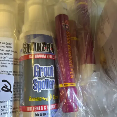 Assortment of household cleaning supplies sealed in a plastic bag, including Stainz-R-Out grout spotter and stain remover pens.