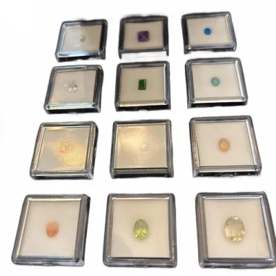 Collection of twelve loose faceted gemstones, including peridot, opal, and amethyst, each presented in an individual clear display case.