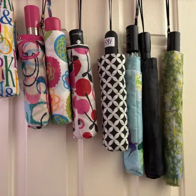 Collection of compact travel umbrellas featuring various colorful patterns, floral prints, and solid colors hanging together on a white...