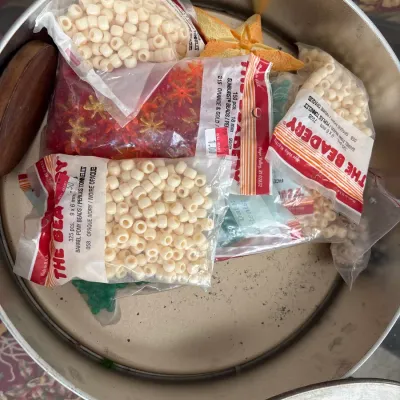 Round metal tin filled with vintage crafting supplies, including packages of plastic pony beads and sunburst beads from The Beadery.