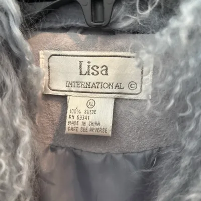 Detail view of the Lisa International brand label on a light blue 100% suede coat with curly shearling trim, size XL.