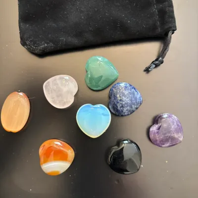 Collection of carved heart-shaped polished gemstones and crystals including amethyst, rose quartz, and lapis lazuli, presented with a...