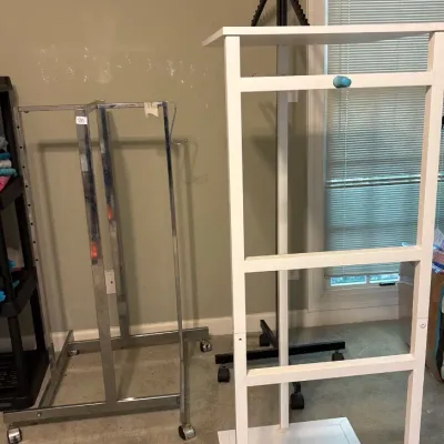 Collection of retail display equipment including a white wooden display tower, a rolling chrome garment rack, and a black stepped rack on...