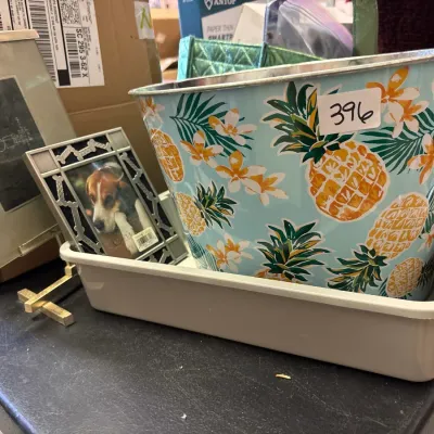 Tropical pineapple-print metal ice bucket sitting in a plastic tray alongside small picture frames.