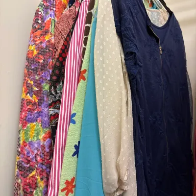 Selection of women's vintage and contemporary clothing hanging on a closet rack, featuring various patterns, textures, and colors.